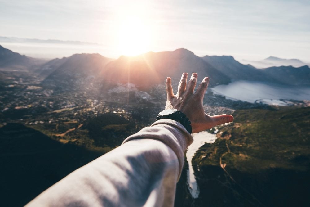 Hand of a man wearing a watch reaching out toward a beautiful landscape in piece about cookieless audience targeting for marketers.