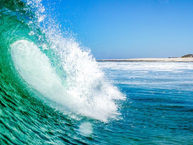 wave in the ocean with the beach visible in the distance