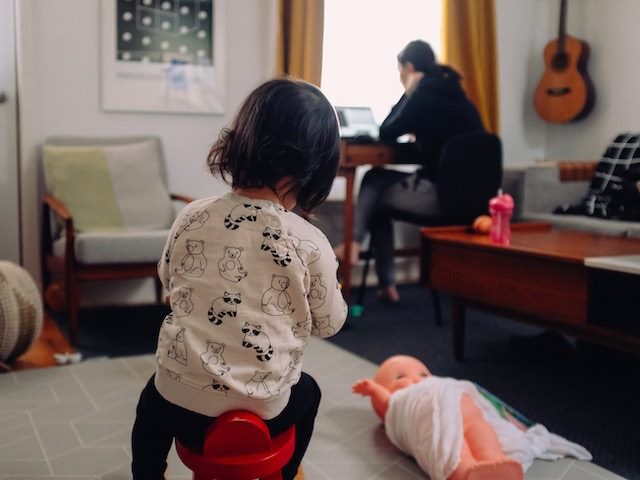 woman working on laptop as child plays in the foreground