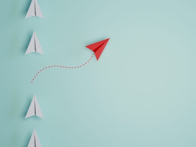 Red paper plane out of line with white papers to represent change and disruption. 