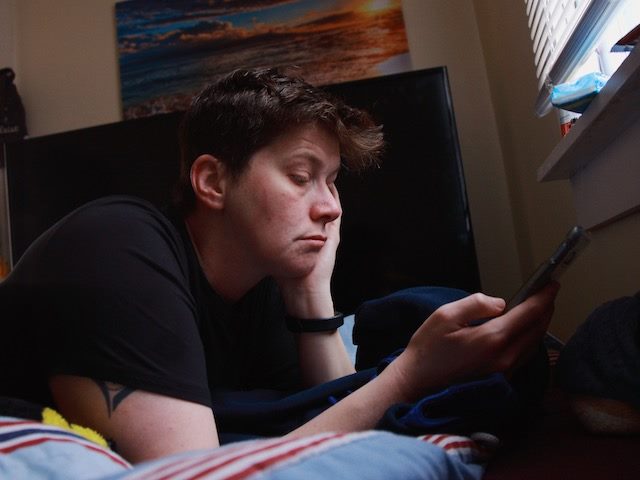 person flopped on their bed, looking at their phone