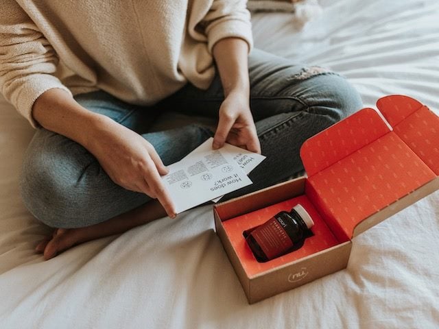 woman sitting cross legged on a bed looking at the contents of a package