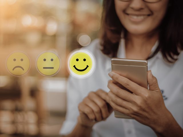 Businesswoman pressing face emoticon on virtual touch screen at smartphone.