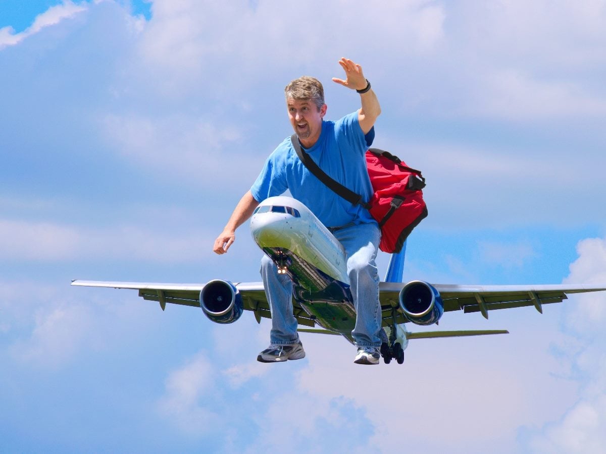 Man with a backpack riding on top of an airplane in midair, symbolizing a packed and fast-moving conference travel season.