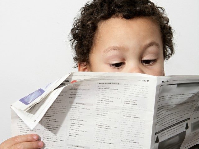 Little boy reading newspaper.