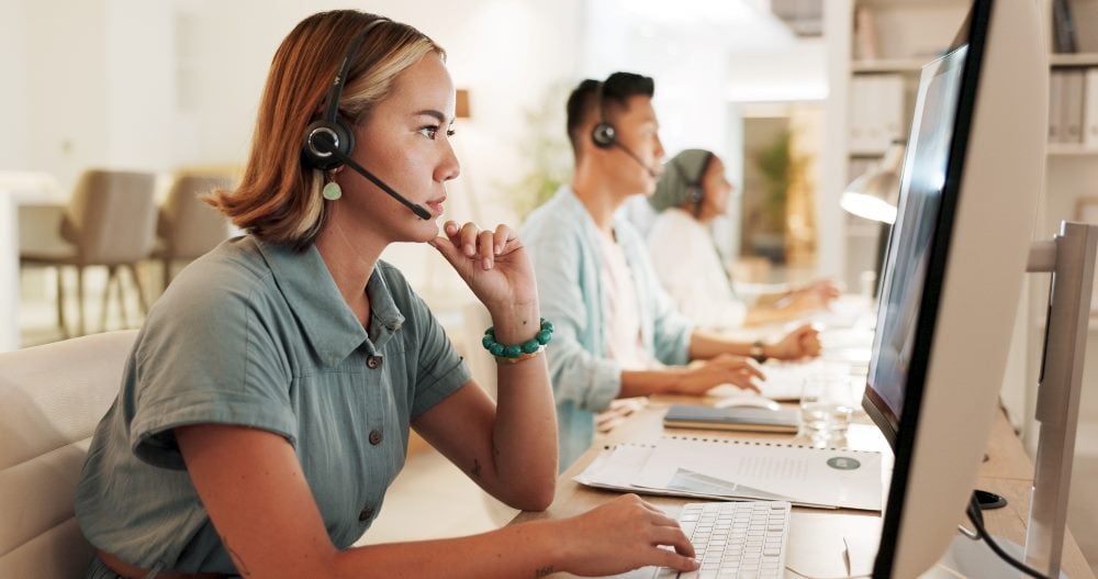 A contact center employee concentrates on helping a customer while working in front of a computer and wearing a headset in a contact center in piece about the synergy between CX and EX.