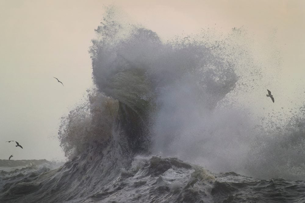 Stormy and powerful waves crash against the cliffs of Cape Disappointment in Ilwaco, Washington, while birds fly above in piece about marking AI turbulence.