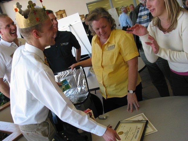 Smiling employees stand around a table. Table has a plaque on it. 