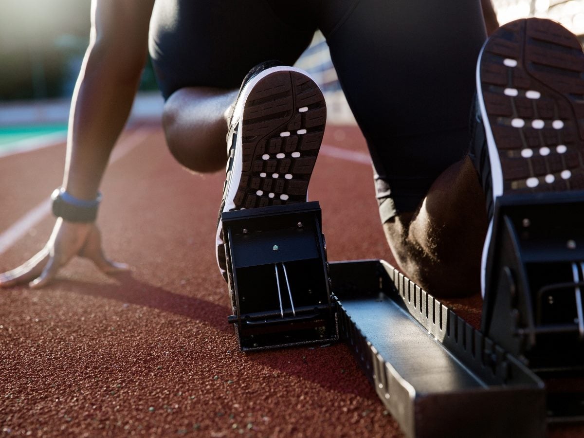 Close-up of a runner in starting blocks on a track, poised to sprint at the starting line, symbolizing preparation and readiness before execution.