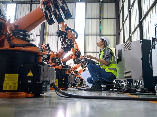 Maintenance engineer, scooting down, looking up at robotic machine automation.