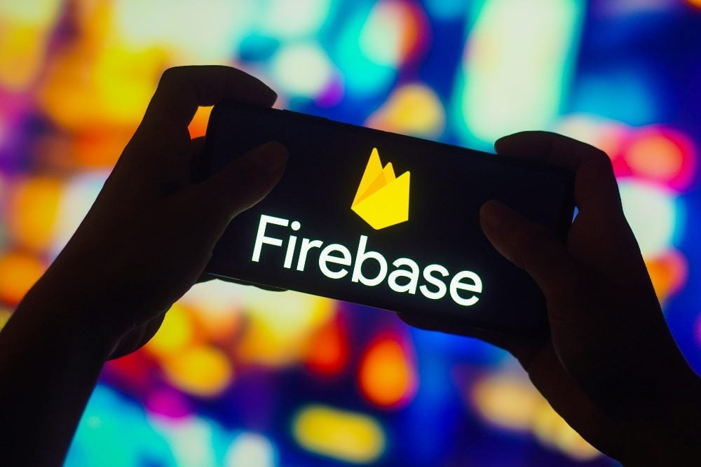 A pair of hands holding a smartphone displaying the Google Firebase Dynamic Links logo against a vibrant, colorful background. The logo features the word "Firebase" with a yellow, flame-like icon above it. The colorful background appears blurred, emphasizing the logo on the phone screen.