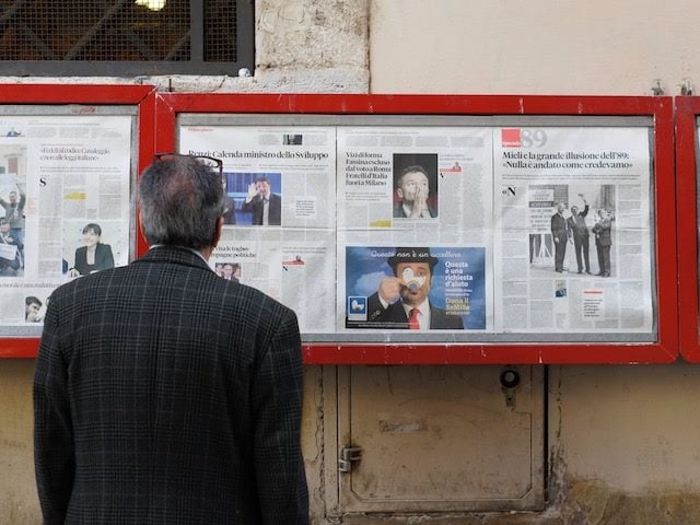man reading newspapers displayed behind glass