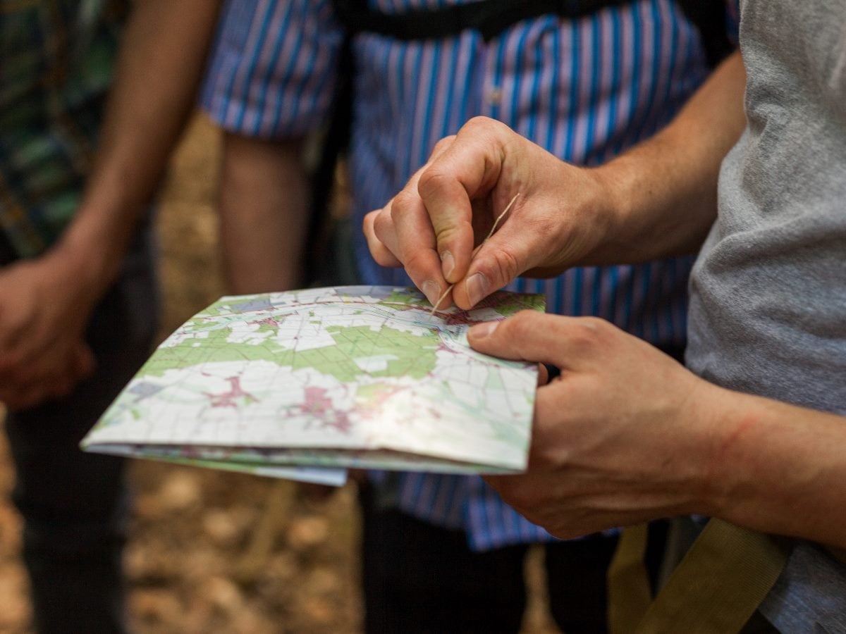 Close-up of a person holding and pointing to a paper map outdoors while standing with a group, suggesting navigation, planning or customer journey mapping.