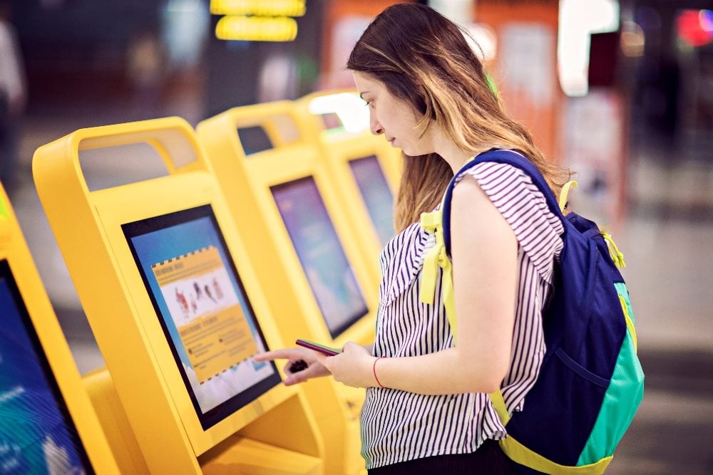 A passenger uses a self-service airline kiosk to check in at the airport in a piece about customer service automation.