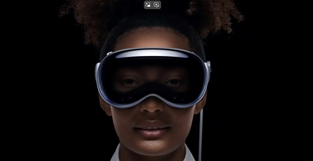 The image features a close-up portrait of a woman wearing a modern, sleek virtual reality headset, called the Apple Vision Pro. The headset covers her eyes and extends slightly above her forehead, resembling futuristic goggles. The background is entirely black, focusing all attention on her and the headset. The woman appears calm and composed, suggesting a serene or immersive experience with the device. In piece about the integration of AI announced at WWDC2024.