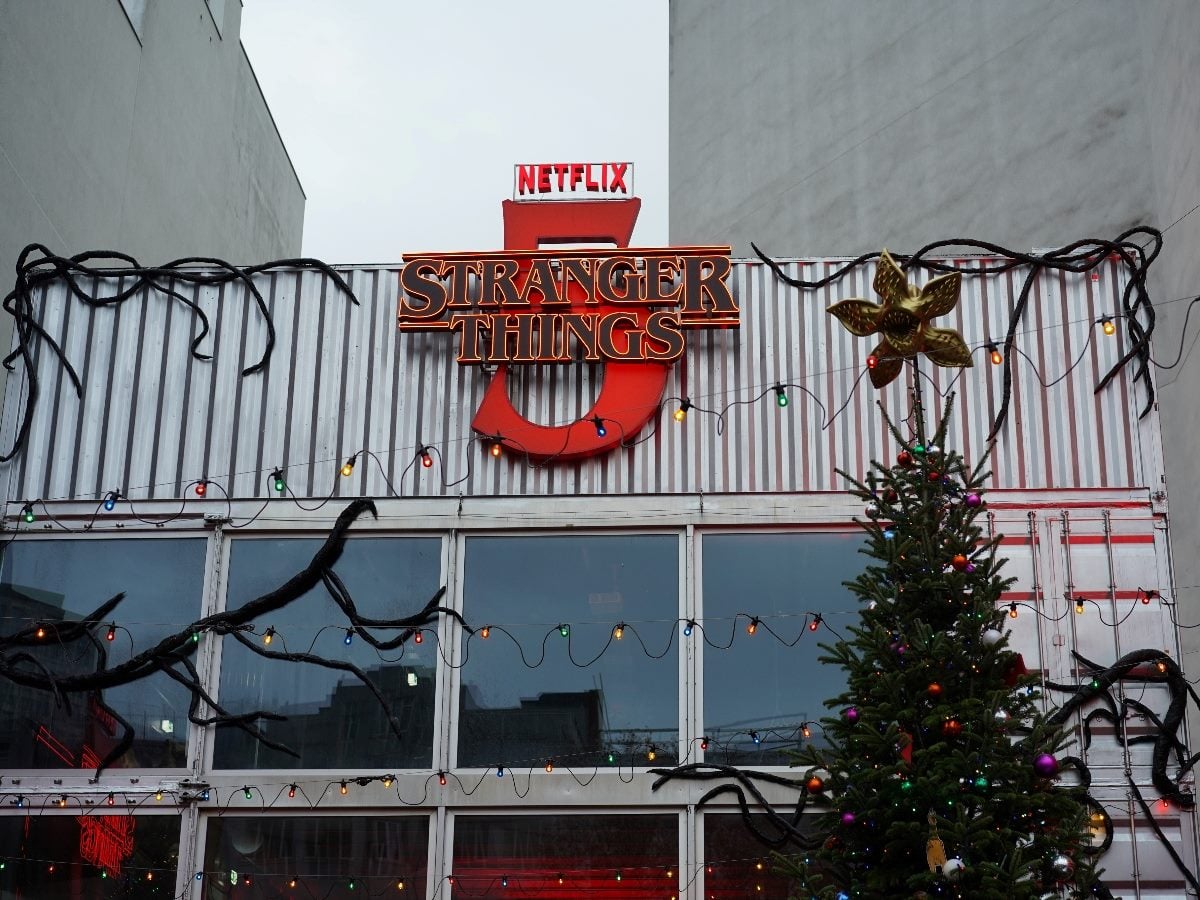 Netflix’s Stranger Things 5 sign mounted on a building facade, decorated with holiday lights and a Christmas tree below, highlighting the franchise’s cultural prominence and Netflix branding.