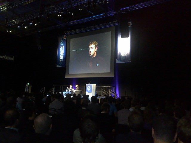 Mark Zuckerberg on stage at a tech conference with a video of him on a big screen behind him.