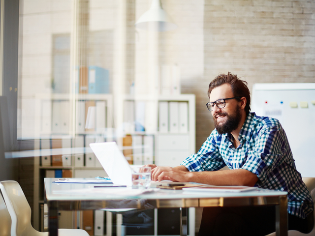 A happy office worker using his computer at a table to complete a task.