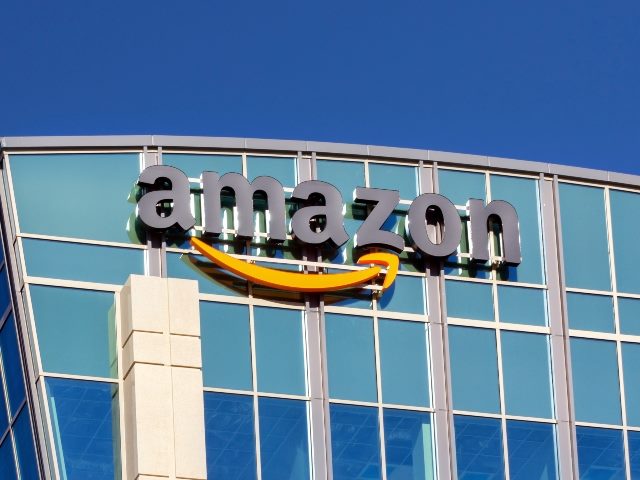 A modern glass and steel building with angled sides and a curved top  with the Amazon company name and logo on its upper left. 