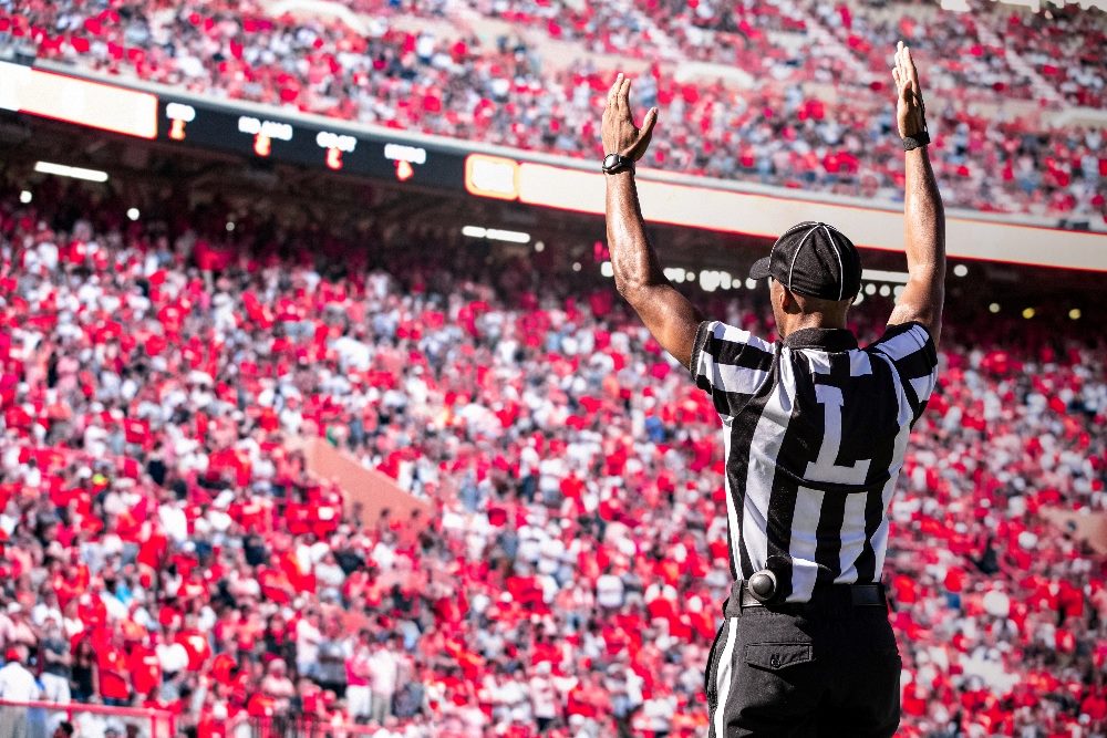 An American football referee holds arms up indicating a touchdown in a large stadium filled with fans in piece about brand authenticity.