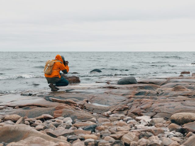 person on a rocky beach in Sweden taking a photo of the horizon 