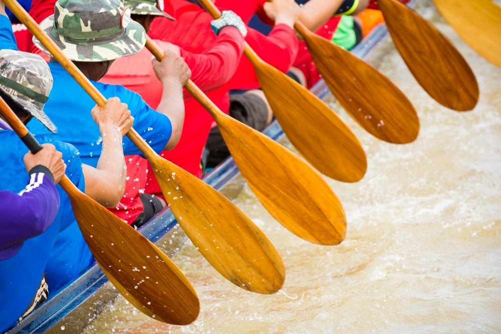 Close up of a rowing team race holding wooden paddles and wearing red and blue shirts in piece about CX and EX.