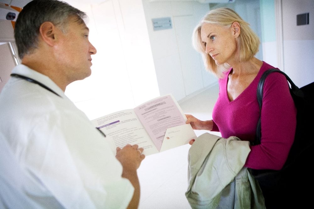A patient discusses her case with her doctor who is holding an open folder in a hospital in piece about digital customer journeys.