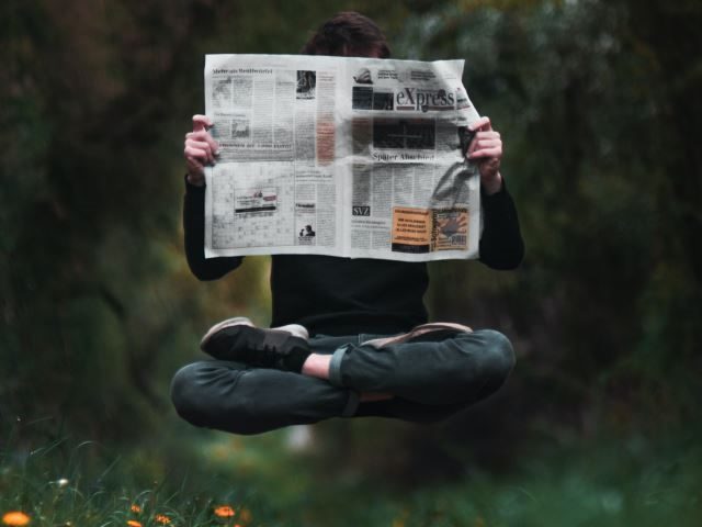 A man in lotus position levitating while reading the newspaper - Workplace Newsbyte