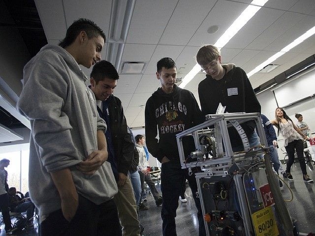 A young man demonstrates technology to a group of other young men.