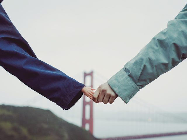person holding hands with a doll hand, golden gate bridge in background