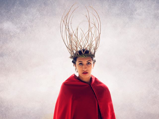 Woman in a red cape with a crown of deer antlers on her head. 