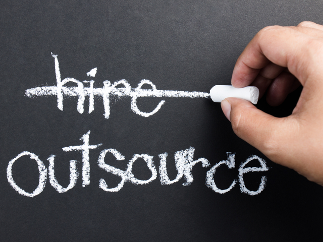Hand writing a line through the word, hire on blackboard with the word outsource written beneath it - outsourcing digital transformation concept