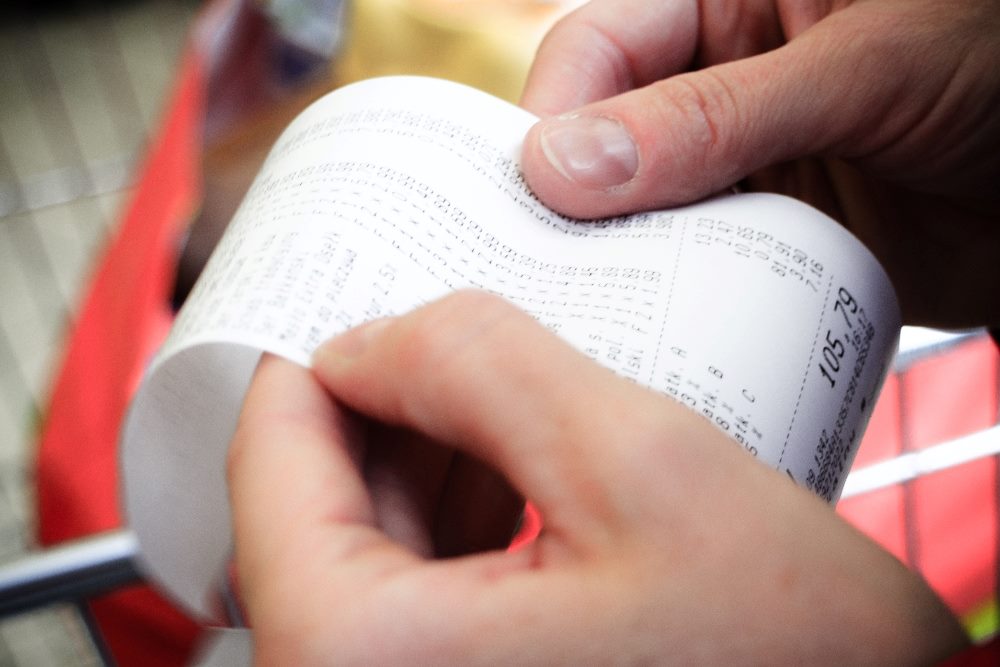 A person holds a store receipt while reviewing prices in piece about pricing strategies.