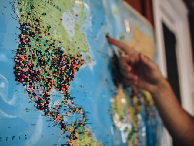 person pointing at map of the world with many pins in it