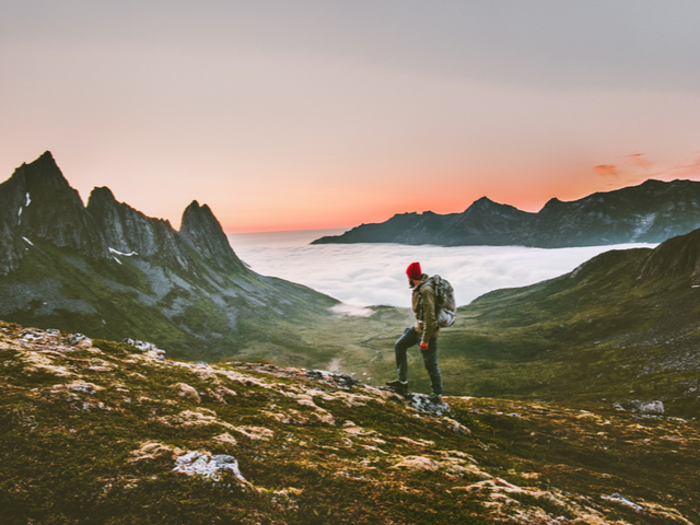 A man walking through the valley surrounded by mountains