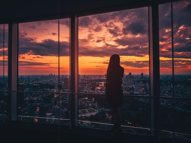 Rear view of woman looking at Tokyo skyline and view of skyscrapers on the observation deck at sunset in Japan.