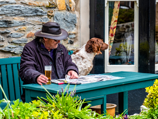 A Man with his dog reading a paper at a cafe