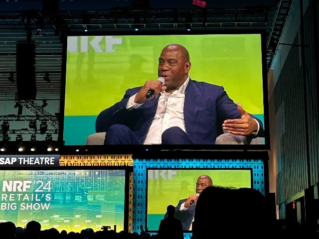 Earvin "Magic" Johnson presents at the National Retail Federation's 20224 "Big Show" in New York City with a bright green background and sitting on a blue couch. 