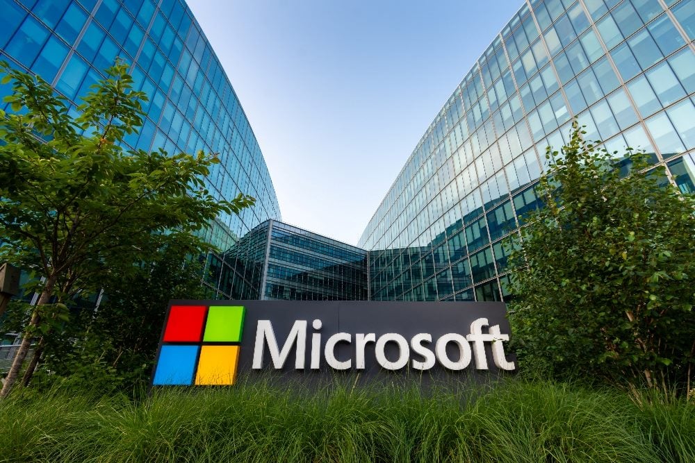 The glass and steel facade of the Microsoft building in Issy-les-Moulineaux, France with greenery in front along with a sign bearing the Microsoft name and logo of four squards in pimary colors of red, blue, yellow and green, in piece documenting generative AI history.