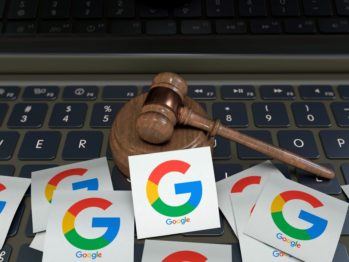 A wooden gavel rests on a laptop keyboard, surrounded by scattered paper cutouts of the Google "G" logo, symbolizing enforcement action tied to Google search rankings.