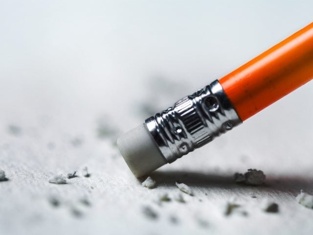 This image shows a close-up of the eraser end of an orange pencil. The eraser is actively being used, with bits of erased material scattered around it on a light surface. The metal ferrule holding the eraser is detailed and slightly tarnished, emphasizing the action of correction in piece about email marketing myths that are wrong. 