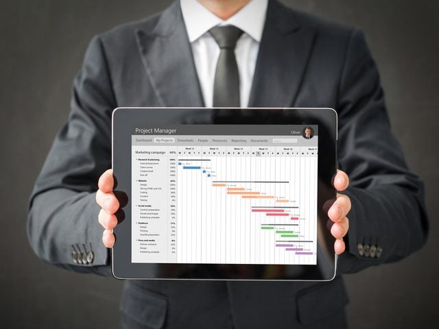 A businessman holding a tablet in both hands presenting a piece of project management software