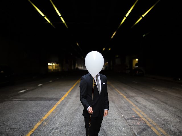 man in business suit hiding face behind a white balloon