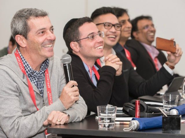 CMSWire DX Summit attendees sitting in a row and laughing as one of them asks a question to a speaker on stage.