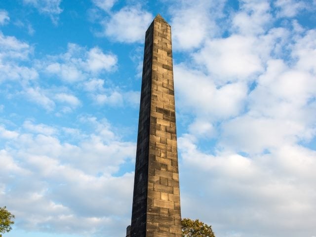 Brick obelisk on the Old Calton Burial Ground in Edinburgh with blue skiy and white clouds in the background.