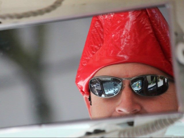 A mirror reflection of a man wearing sunglasses and a red hat.