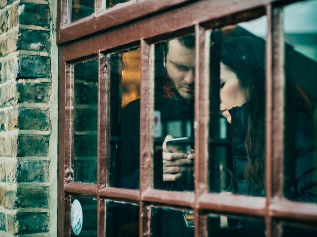 two people using a phone behind a window in a brick wall