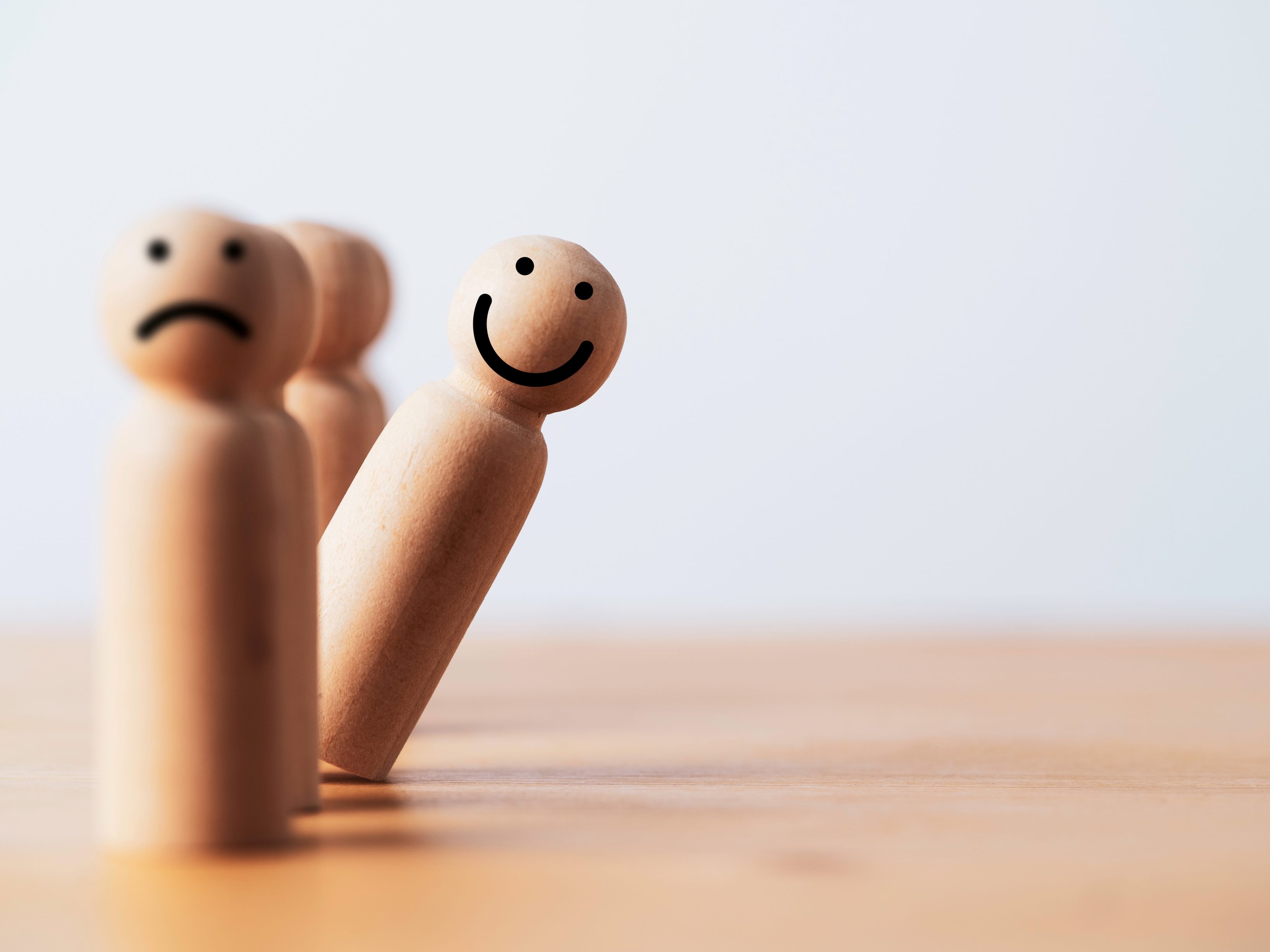 Wooden pegs in a row one with a sad face and one leaning out with a happy face suggesting the potential for AI in CX to be either good or bad.