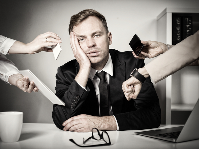 Businessman feeling overwhelmed at work, with several varying hands holding different (technologies, phone, digital watch, tablet, etc.) in his face.