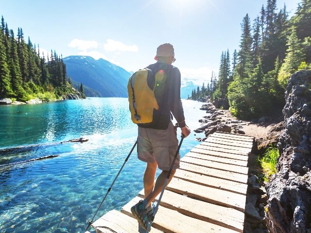 A hiker in hiking gear and carrying a backpack hikes along a wooden path alongside Garibaldi lake in British Columbia in Canada in piece about the B2B buying journey. 